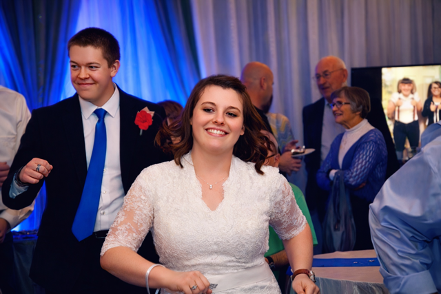 Bride and groom smiling and dancing at their wedding reception surrounded by guests.