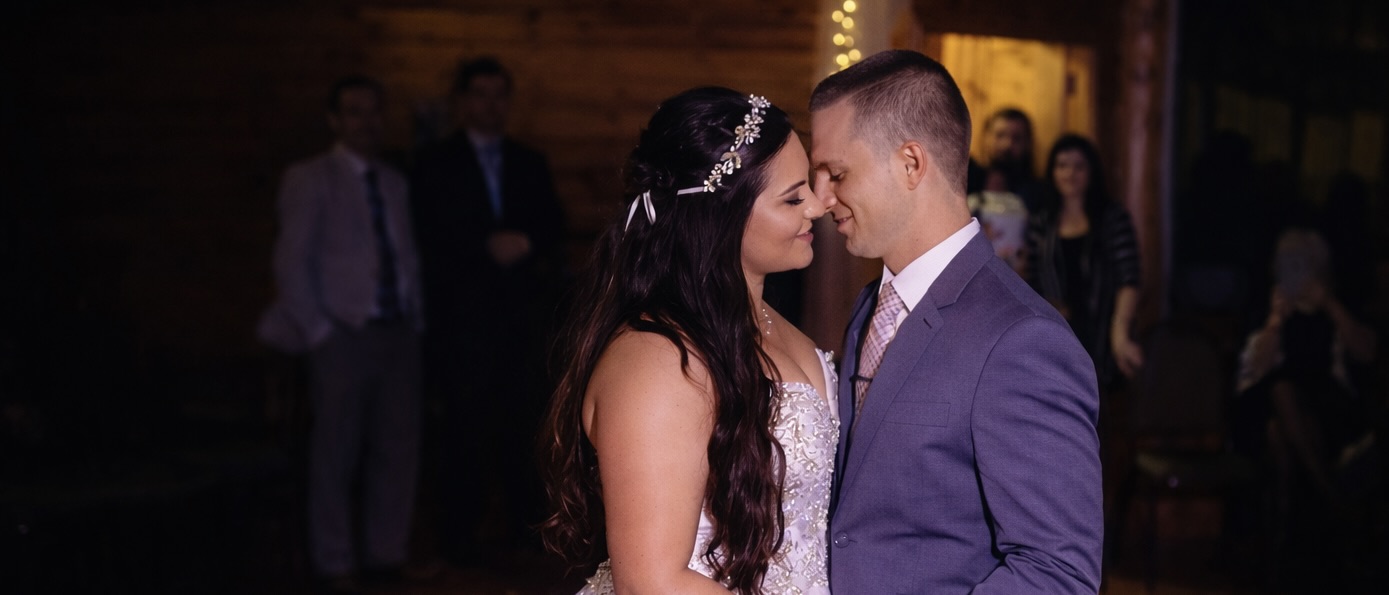 Newlywed couple holding hands during their first dance at an intimate barn wedding reception with string lights.