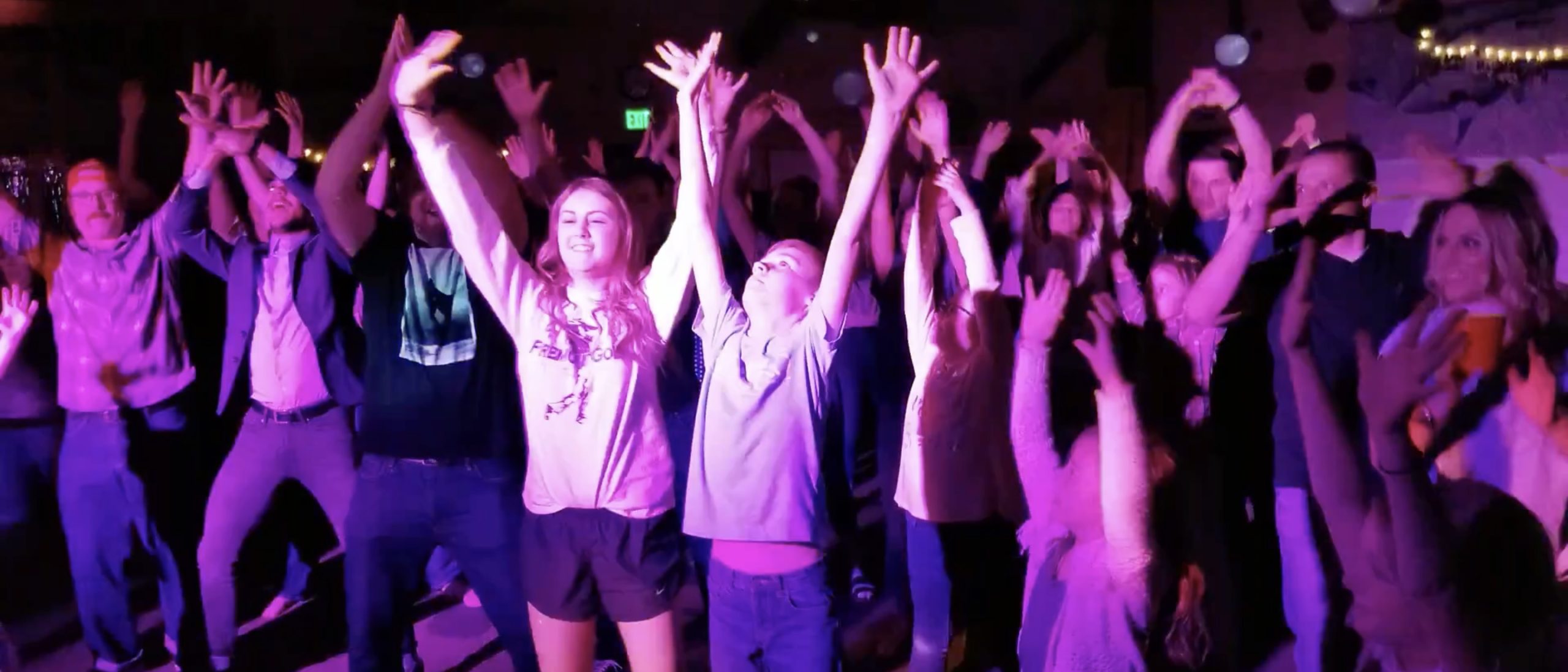 High-energy DJ services with a packed dance floor and guests dancing under colorful event lighting.