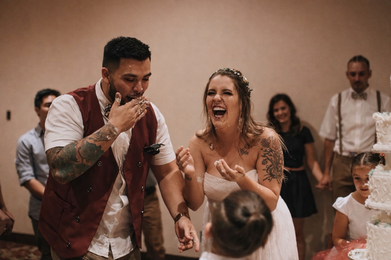 Utah Wedding DJ & Photo Booth | America's Wedding DJ Laughing bride and groom doing a fun cake smash at their Utah wedding reception, covered in cake and full of joy.